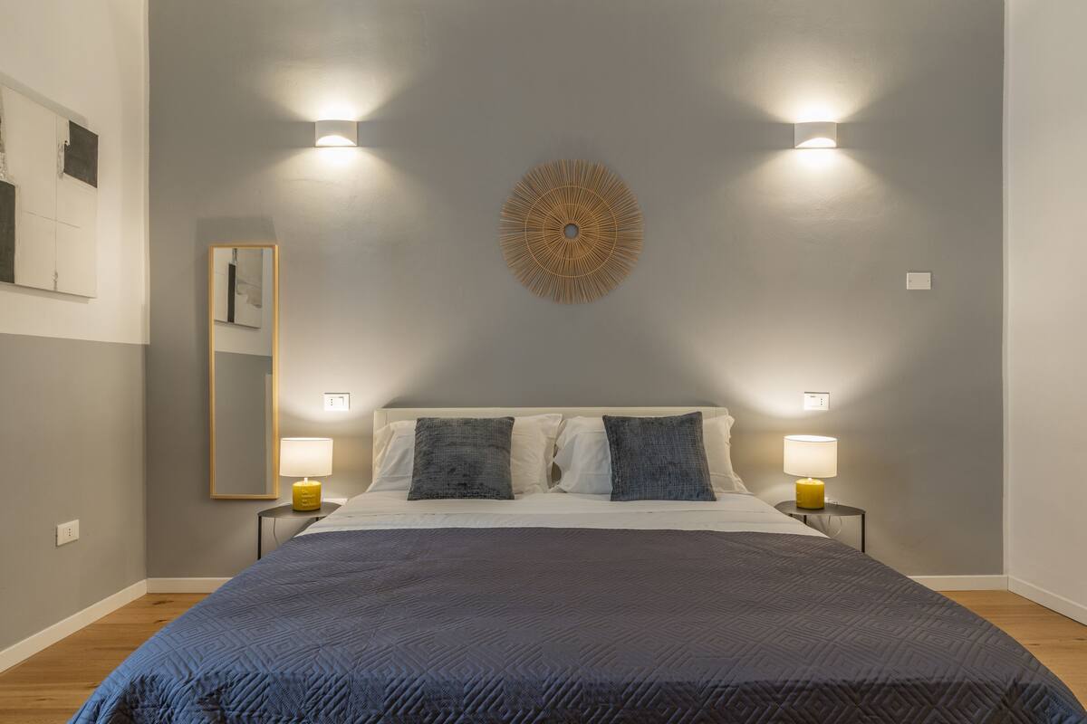 Une chambre à coucher avec un grand lit, deux lampes de chevet, un luminaire fixé au mur et un miroir.