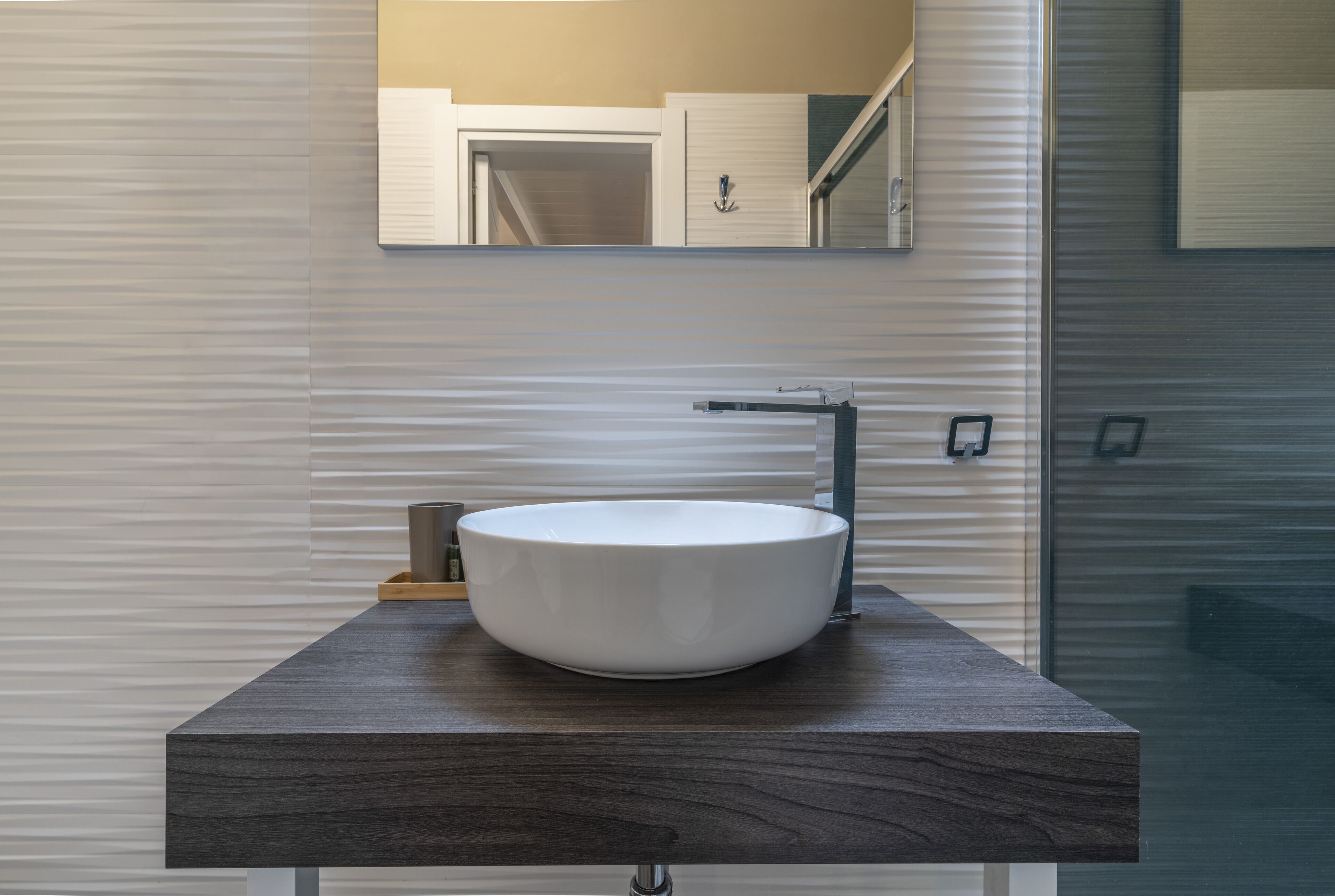 Un bagno moderno con un mobile lavabo in legno scuro, un lavabo a vasca bianca e uno specchio soprastante.