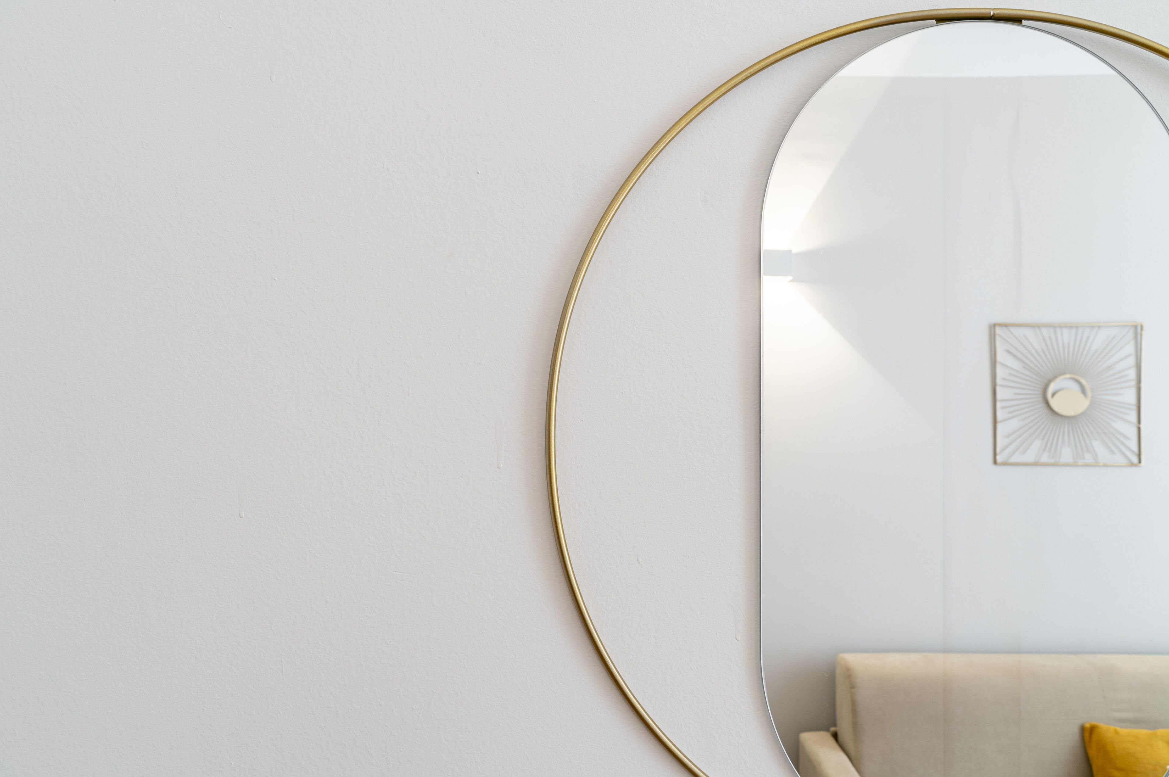 A minimalist room with a round mirror, a light-colored wall, and a sofa with a yellow pillow.