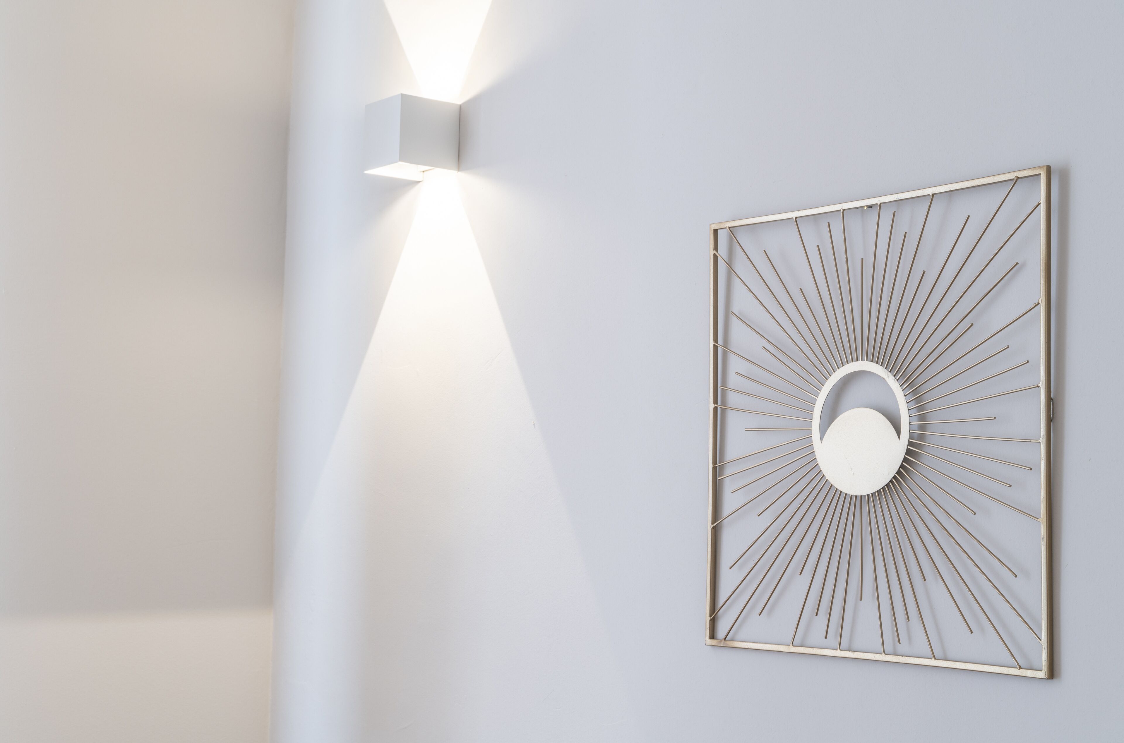Una lámpara de pared con forma de sol naciente, con un elemento circular central y un marco geométrico.