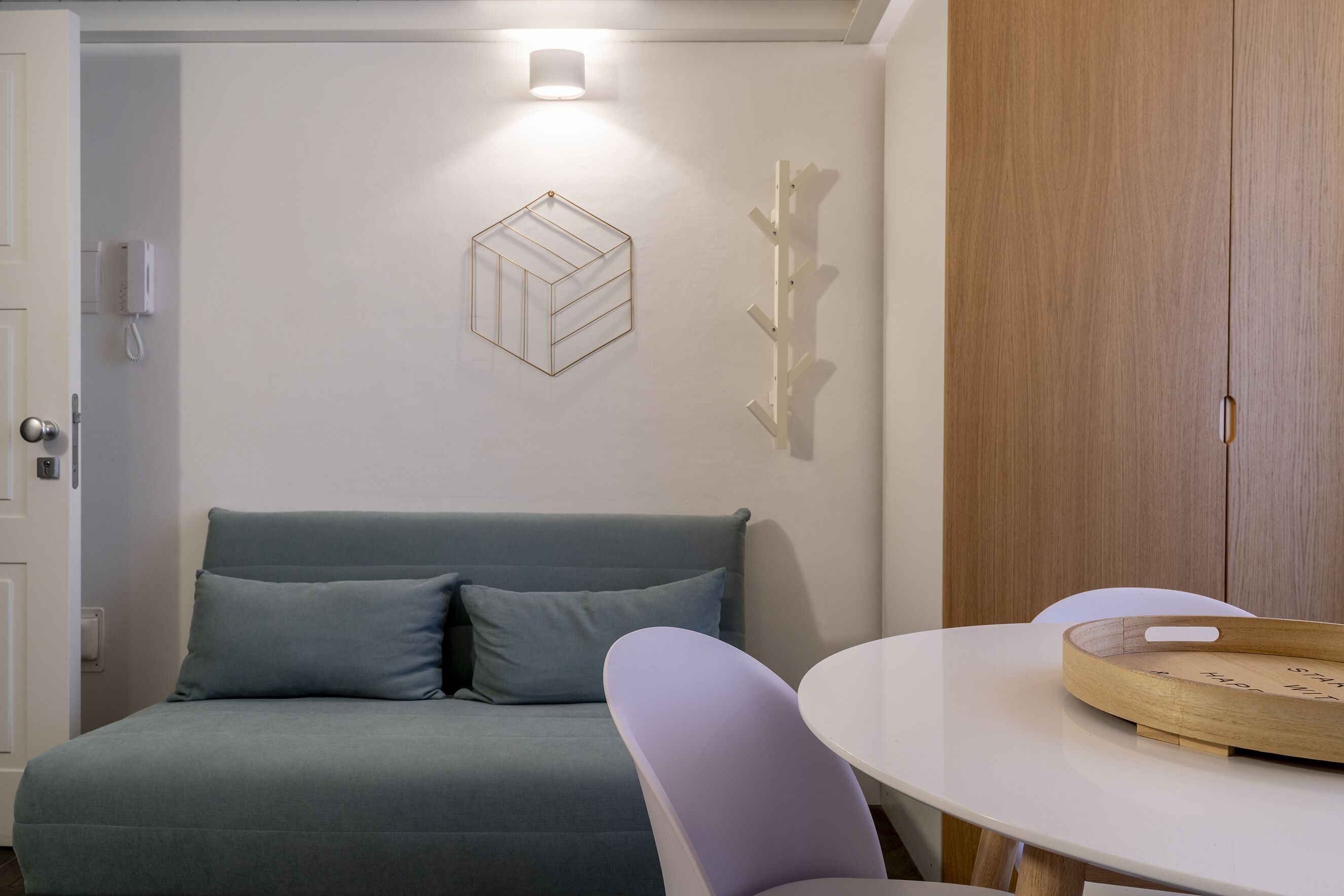 Un dormitorio con cama, mesita de noche, una silla, armario e iluminación en la pared.
