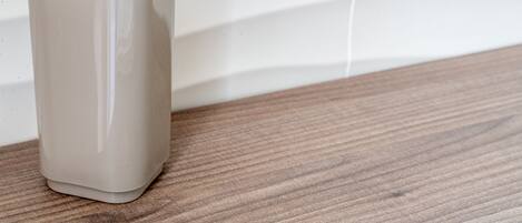 A beige ceramic vase on a wooden surface against a white tiled wall.