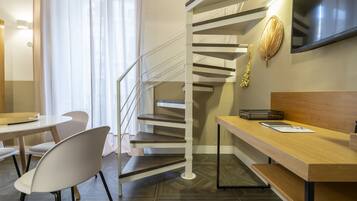 A modern hotel room with a spiral staircase, a wooden desk, and a flat-screen TV mounted on the wall.