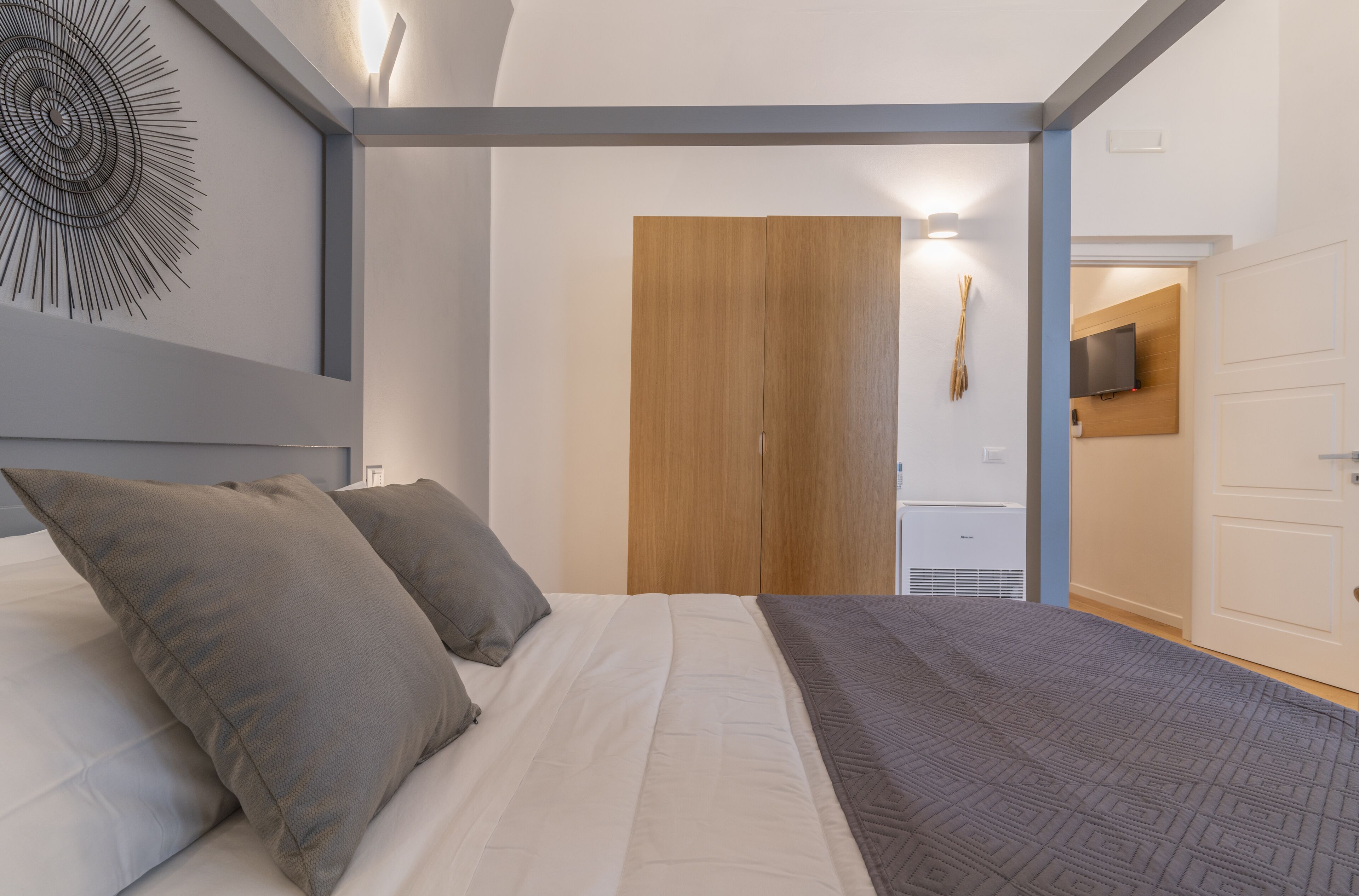 Una camera da letto con un letto, cuscini, un'armadio in legno e un televisore appeso al muro.