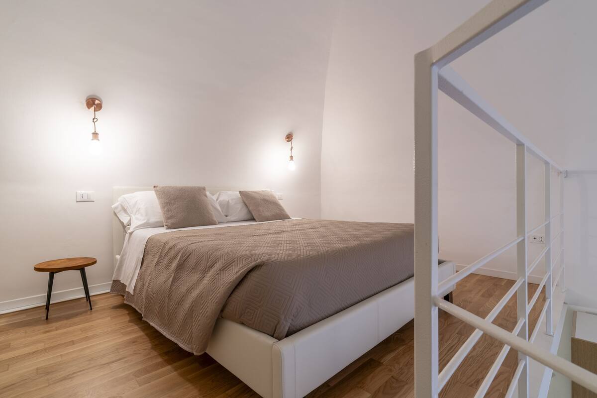 Une chambre à coucher avec un lit, un petit tabouret en bois et deux lampes fixées au mur.