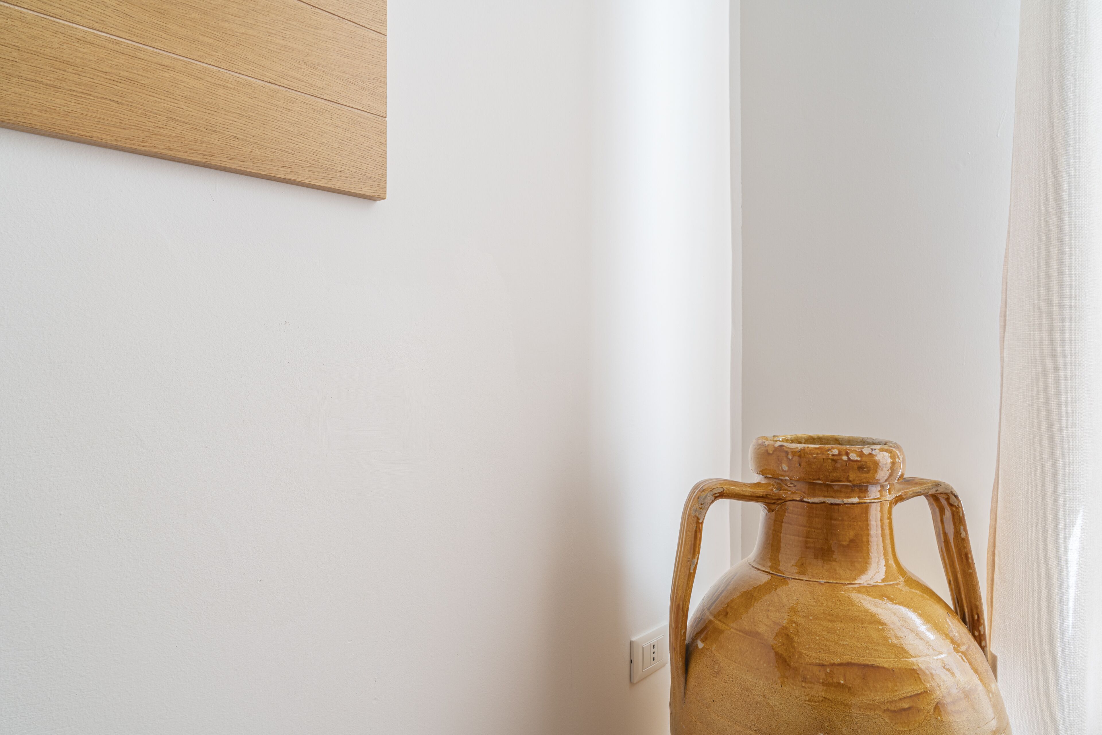 A ceramic jug with a handle, placed against a white wall next to a wooden panel and a light switch.