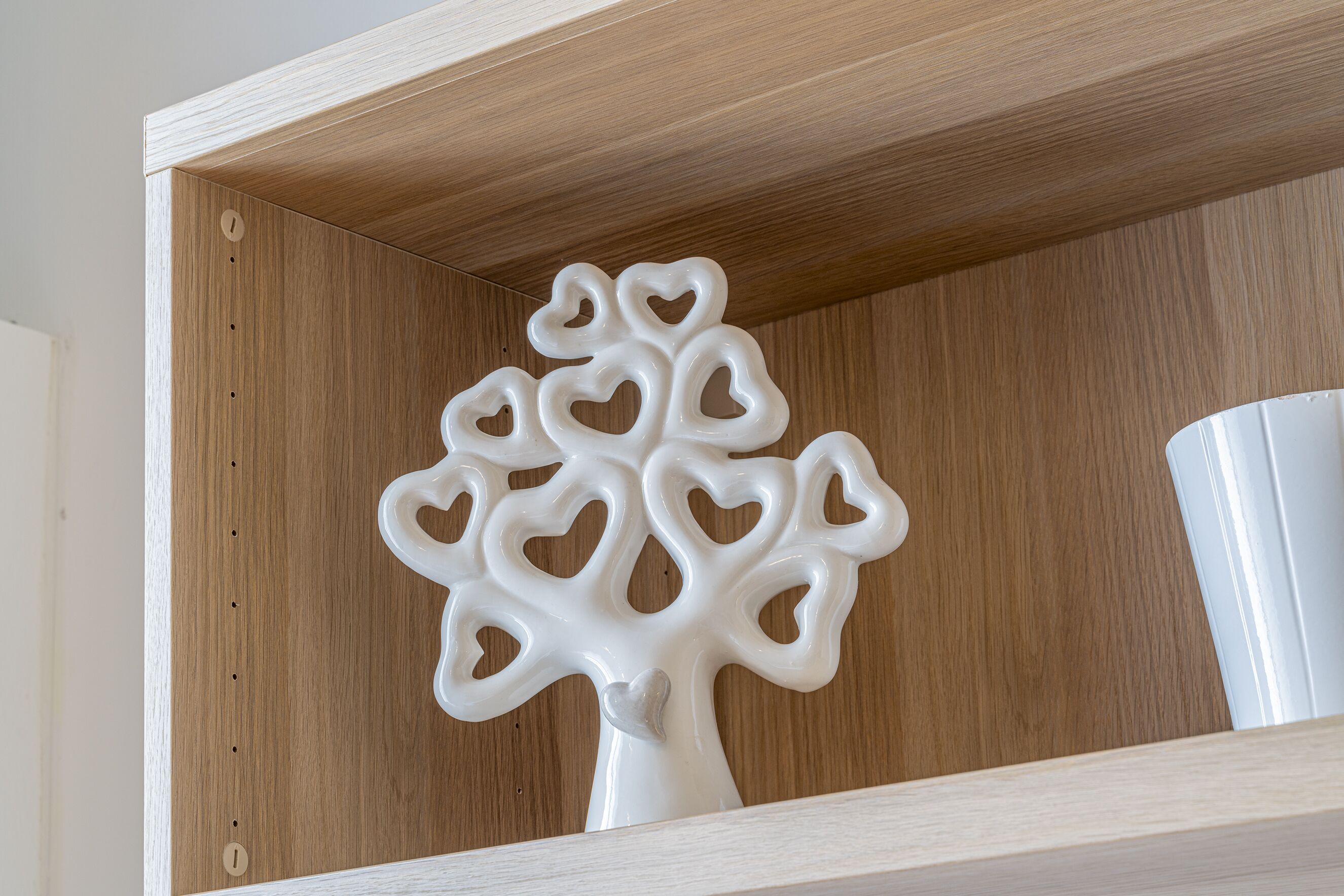 A white ceramic tree with heart-shaped cutouts on a wooden shelf.