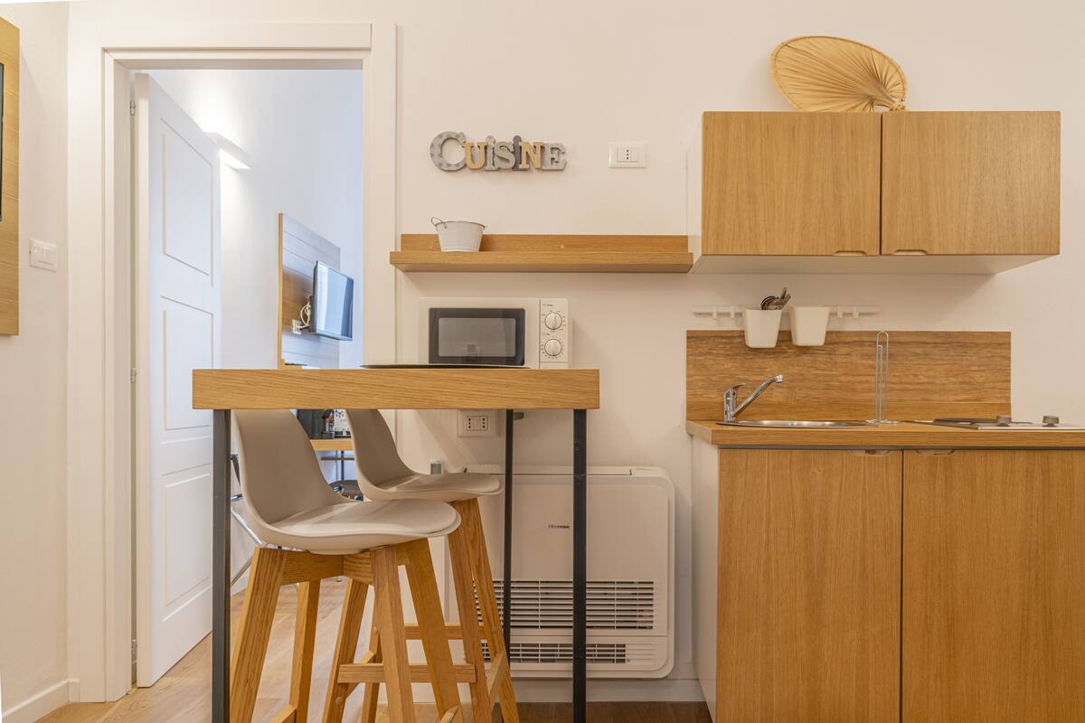 Une petite cuisine équipée avec des meubles en bois, un four à micro-ondes, un évier et un petit tabouret de bar.