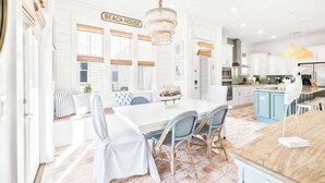 A modern kitchen with a white island, a dining area with a white table and chairs, and a sign reading 'BEACH HOUSE'. - Coastal Oasis by Stay on 30a (Inlet Beach)