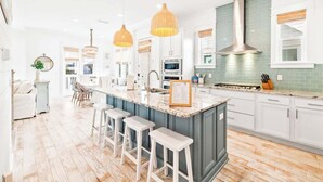 A modern kitchen with a central island, bar stools, pendant lights, and a stainless steel range hood. - Coastal Oasis by Stay on 30a (Inlet Beach)