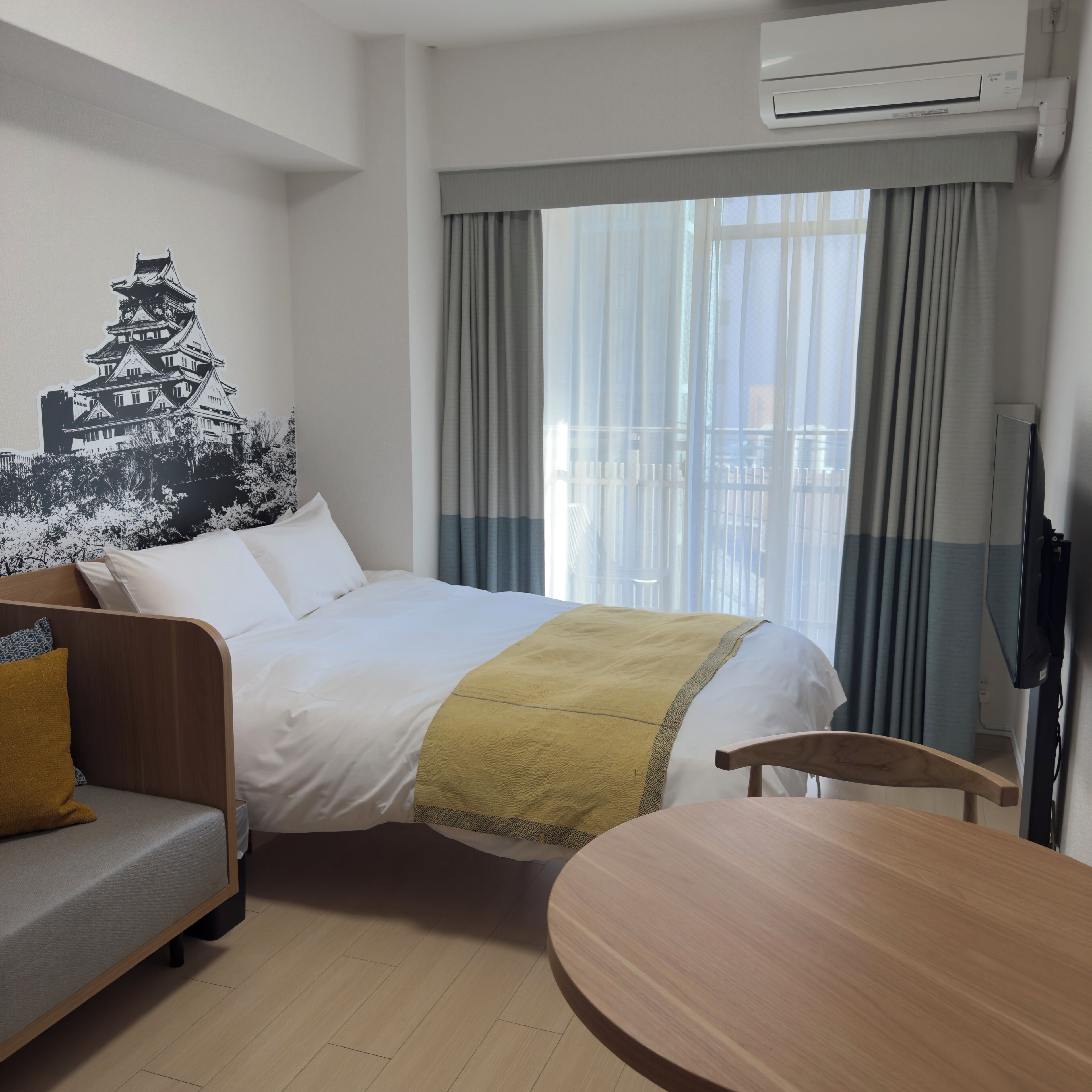 A hotel room with a bed, a sofa, a TV, and a window with curtains.