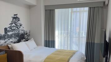 A hotel room with a bed, a sofa, a TV, and a window with curtains.