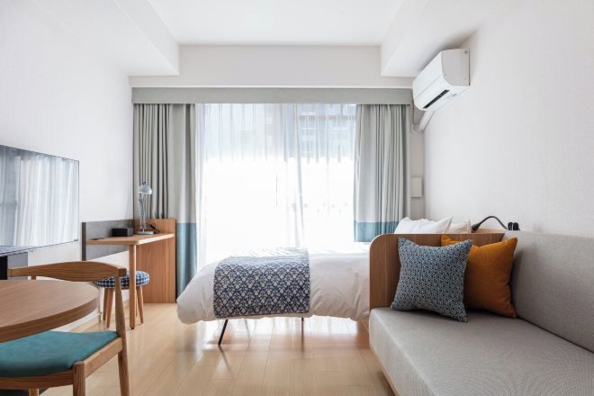 Een moderne hotelkamer met een bed, een bank, een televisie, een bureau en een raam met gordijnen.