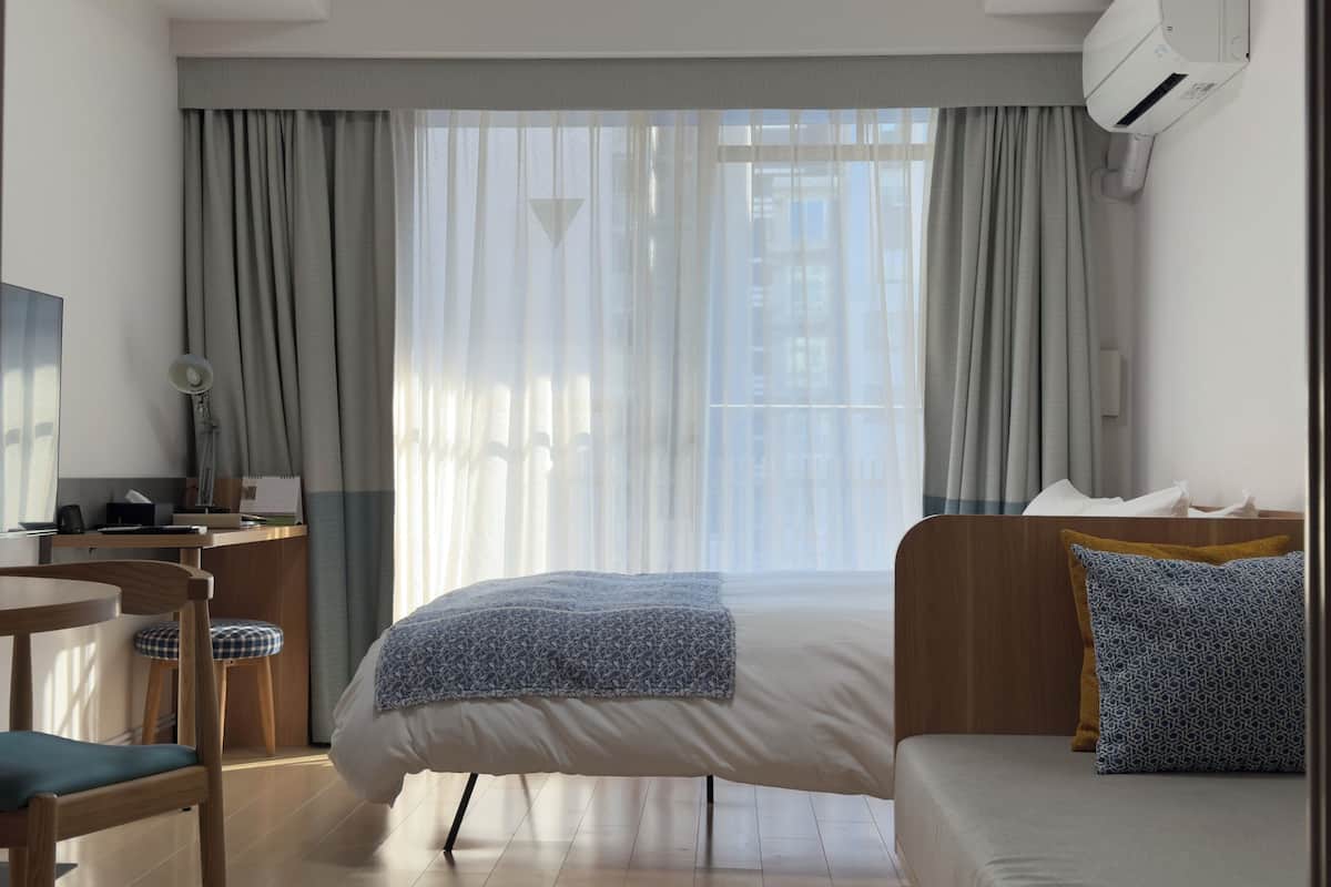 Ein Hotelzimmer mit einem Bett, einem Schreibtisch mit Stuhl, einem Fernseher und einem Fenster mit Vorhängen.