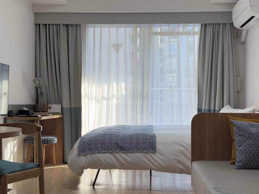 A hotel room with a bed, a desk with a chair, a TV, and a window with curtains.