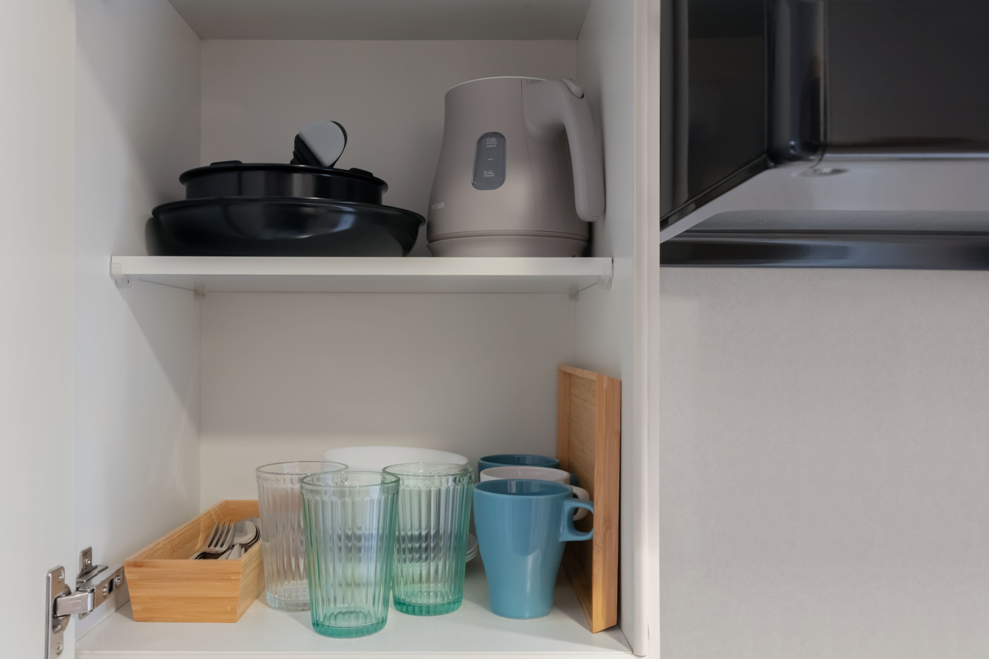 A kitchen shelf with a kettle, pots, and glasses.
