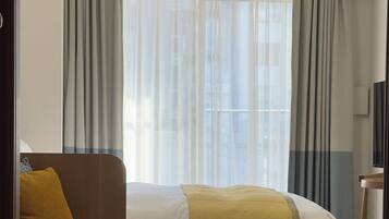 A modern hotel room with a bed, a sofa, a TV, and an air conditioning unit.