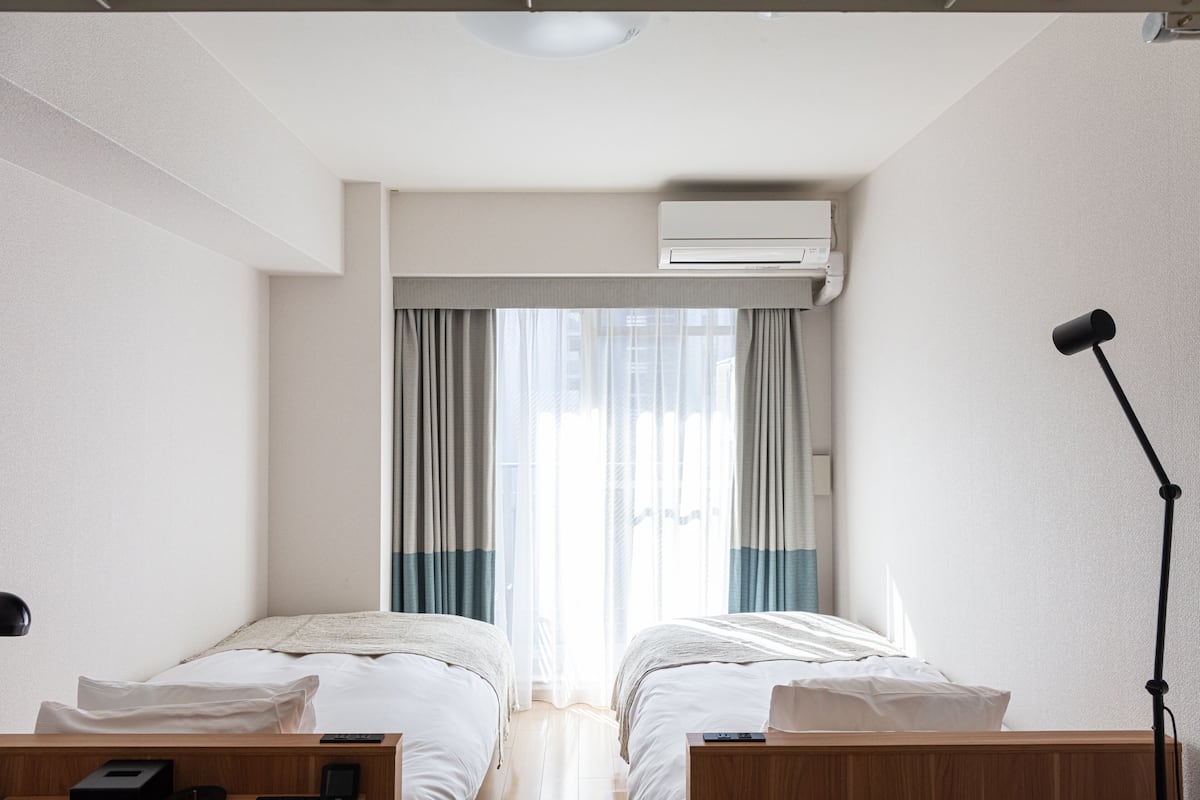 Ein Hotelzimmer mit zwei Betten, einem Schreibtisch, einer Lampe und einer Klimaanlage.