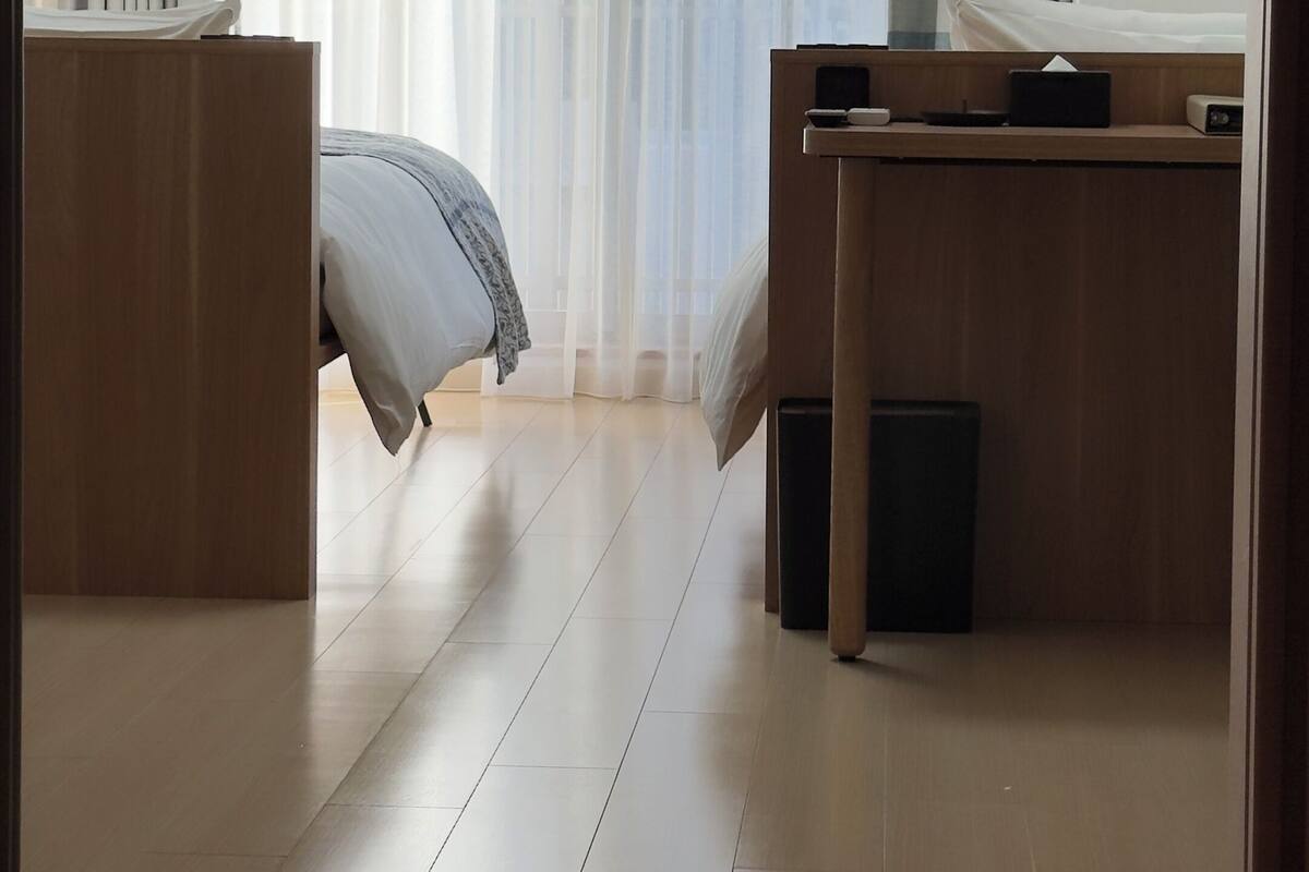 Ein Hotelzimmer mit Bett, Schreibtisch, Klimaanlage und Blick ins Freie durch transparente Vorhänge.