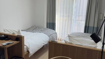 Habitación de hotel con dos camas, un escritorio, una silla, un cesto de basura y un equipo de aire acondicionado.