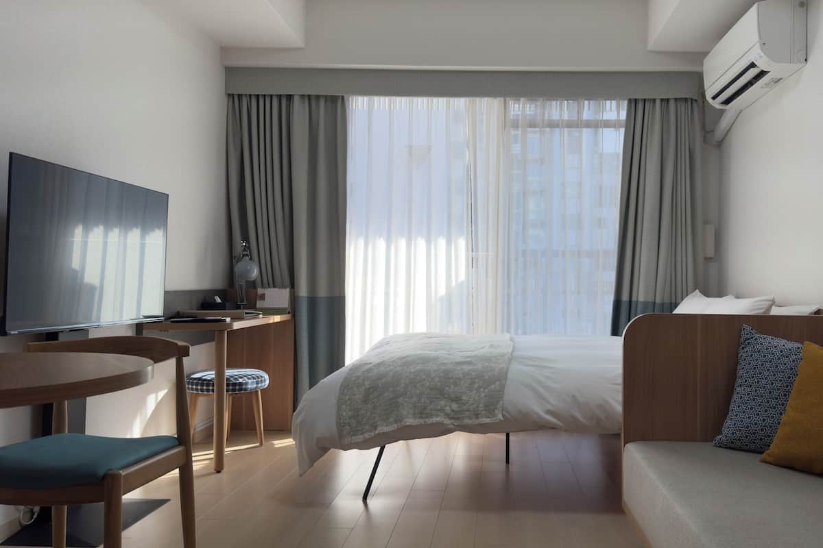 Ein Hotelzimmer mit Bett, Sofa, Schreibtisch mit Stuhl, Fernseher und Klimaanlage.