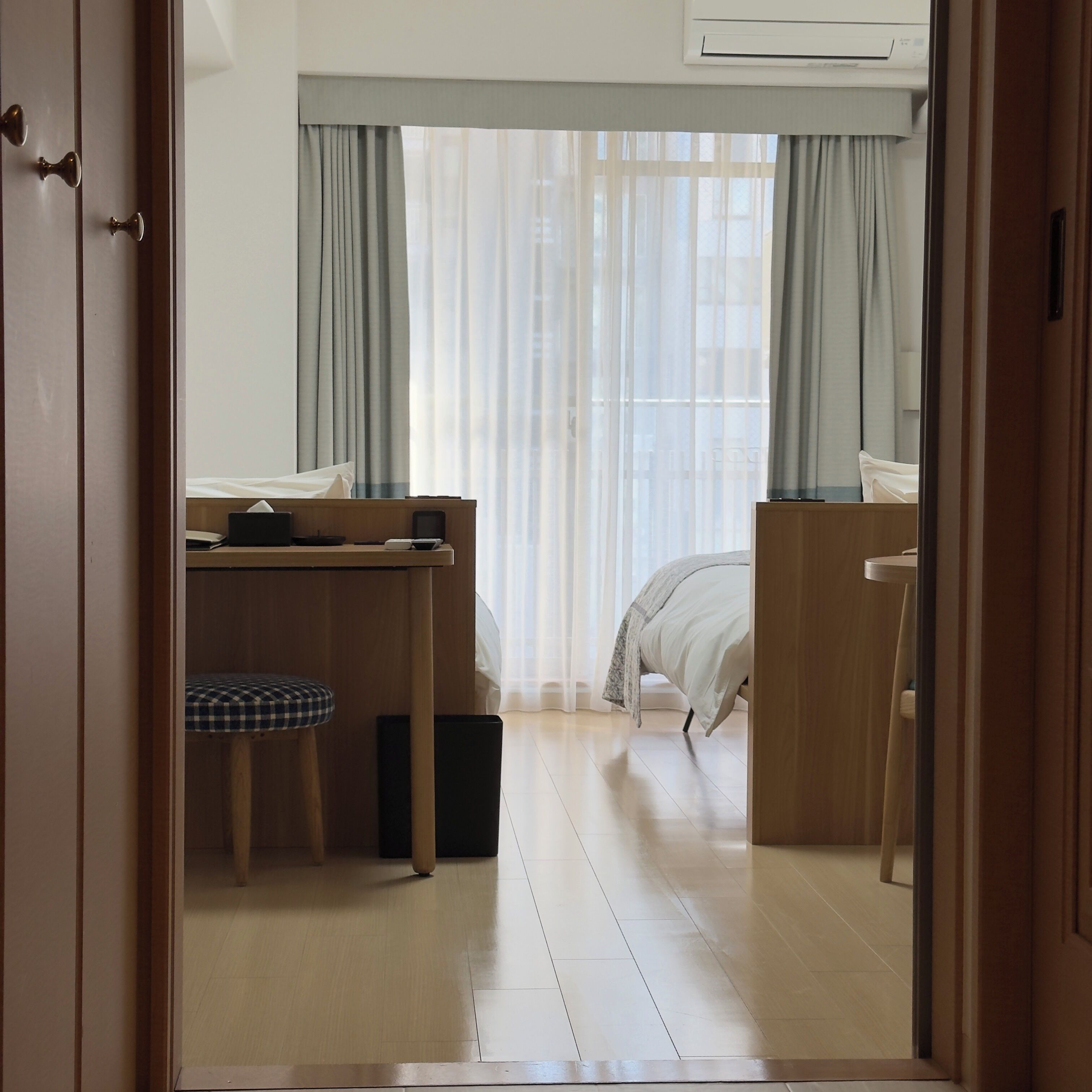 A hotel room with a wooden desk, a chair, a bed, and a large window with sheer curtains.