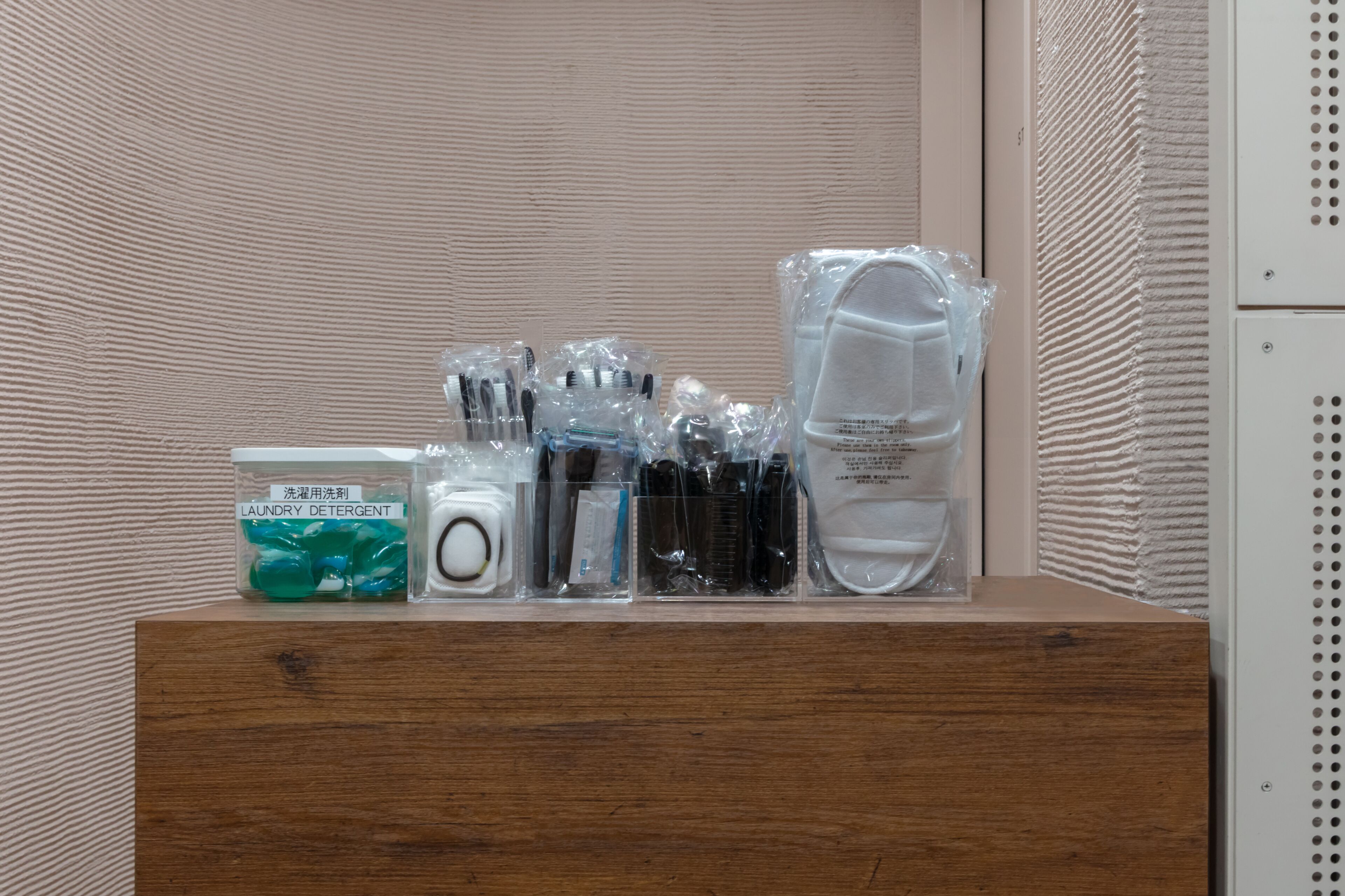 Une étagère en bois sur laquelle sont rangés divers produits de toilette, notamment un bidon de lessive, un appareil photo et d’autres articles de soins personnels.
