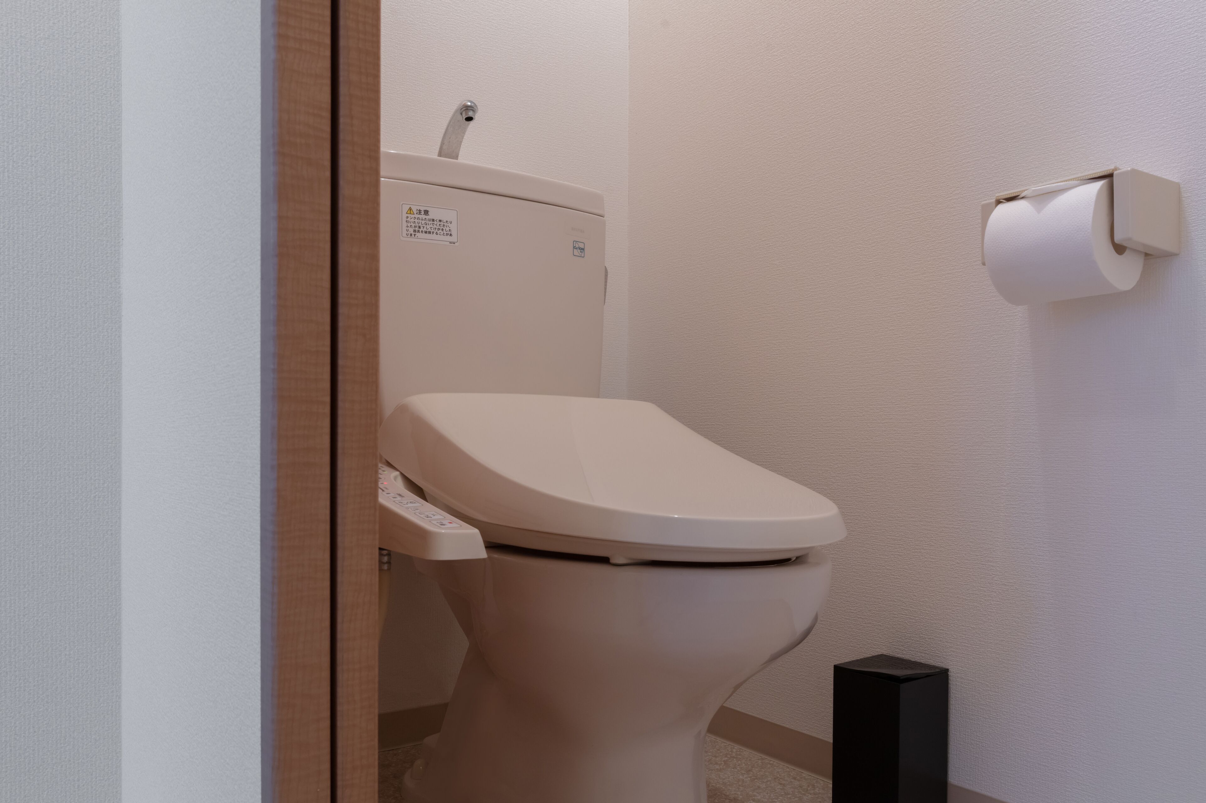 Een moderne toilet met een bedieningspaneel, een toiletrolhouder aan de muur, en een zwart object op de vloer.