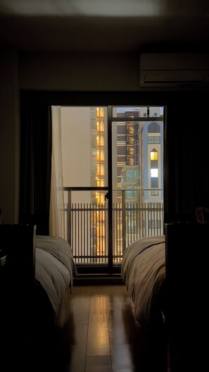Ein Hotelzimmer mit zwei Betten, einem Balkon mit Blick auf die Stadt und einem Fenster mit Vorhang.