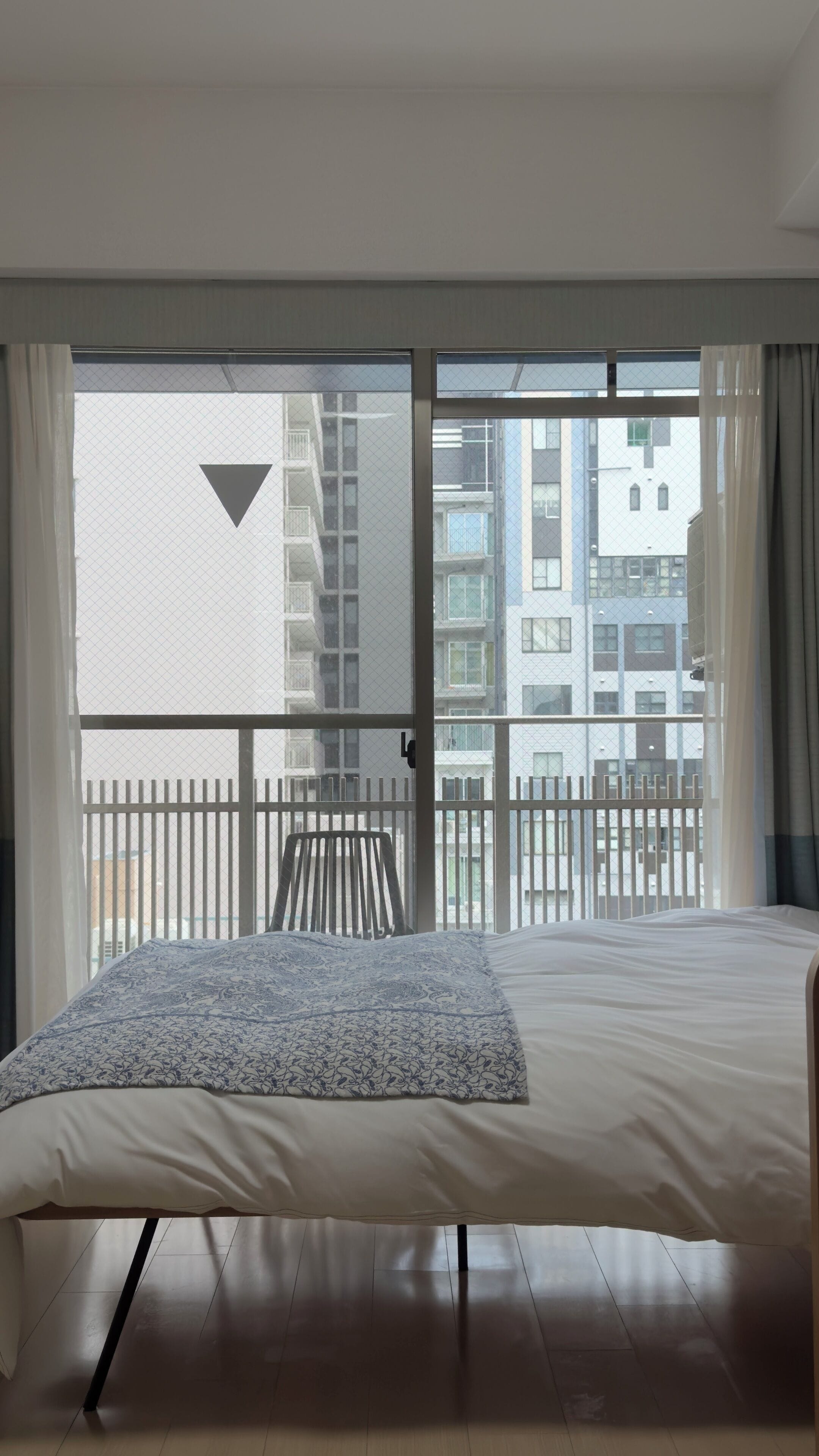 A bedroom with a bed, a large window, and a view of a balcony with a railing.
