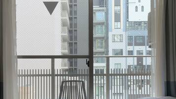 A bedroom with a bed, a large window, and a view of a balcony with a railing.