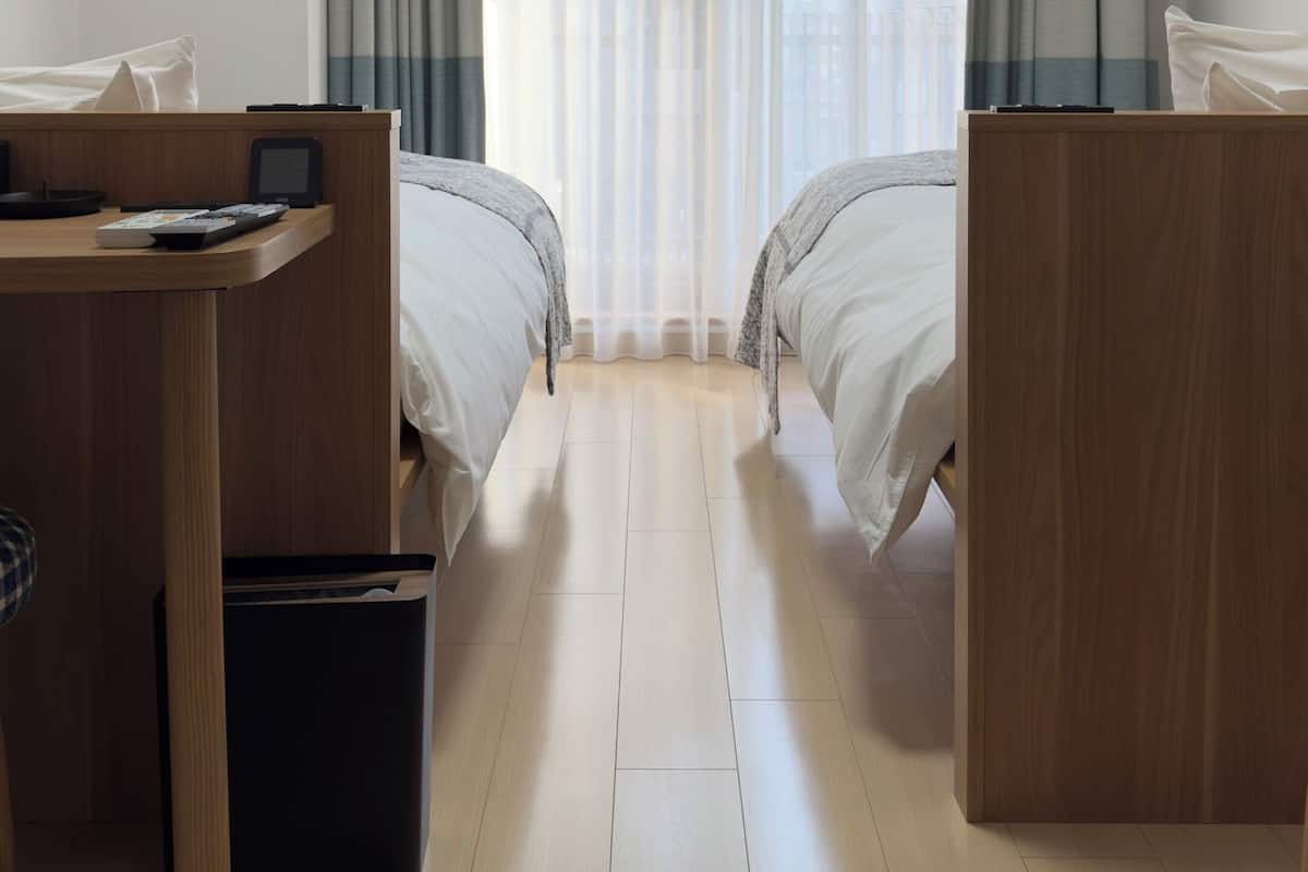 Ein Hotelzimmer mit zwei Betten, einem Schreibtisch, einem Mülleimer und einer Klimaanlage.