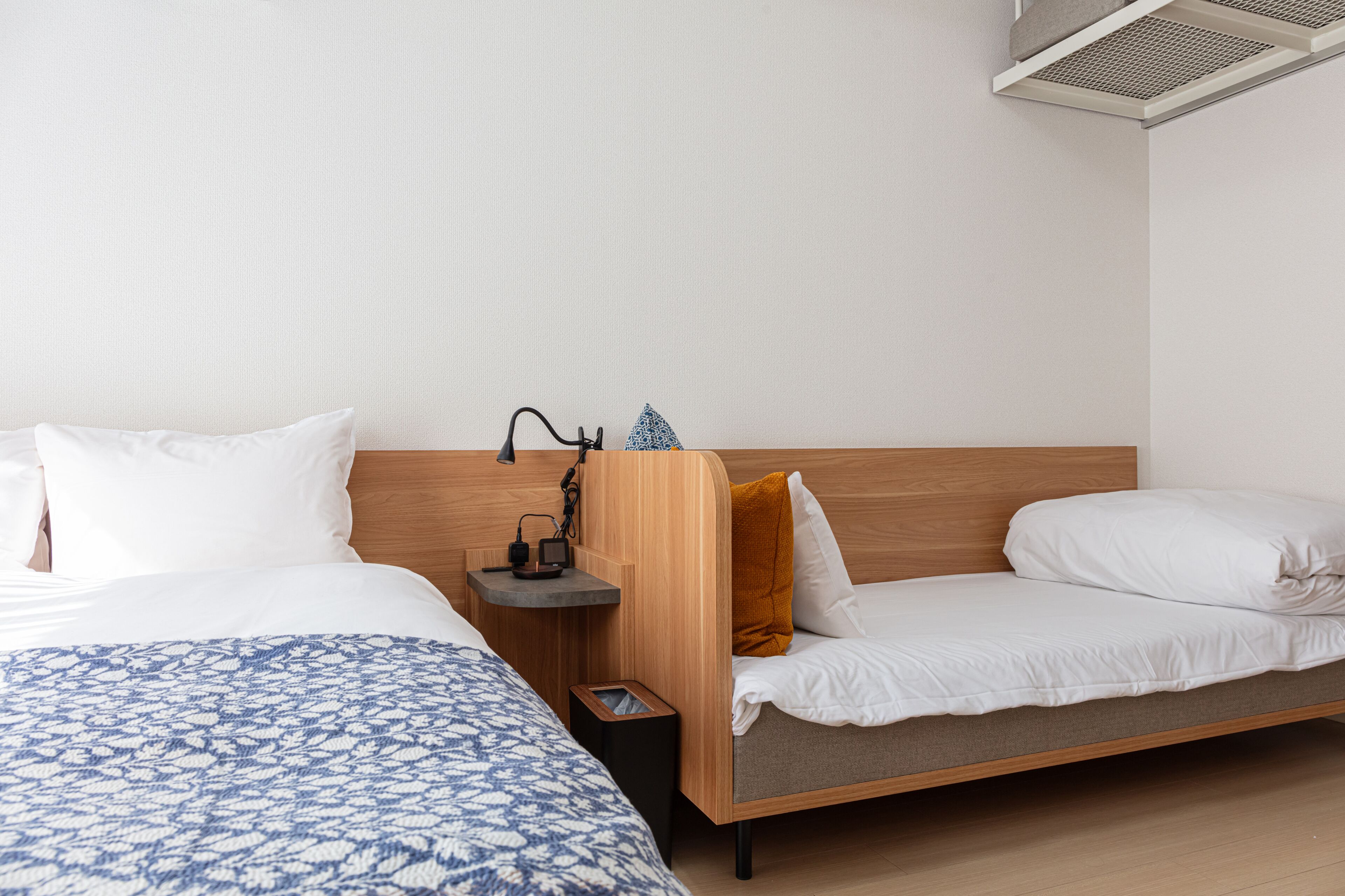 A modern hotel room with a wooden headboard, a bedside table with a lamp, and a small nightstand.