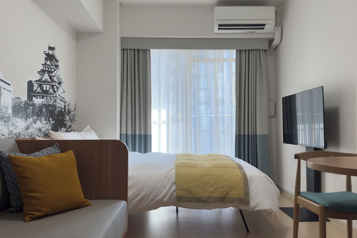 Ein Hotelzimmer mit Bett, Sofa, Fernseher und einem Vorhangfenster.