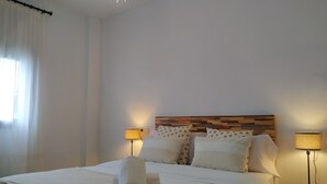 A neatly made bed with white linens and a rolled towel, two bedside lamps, and a wooden headboard. - Condo Entero en Pantano de los Bermejales (Pantano de los Bermejales)