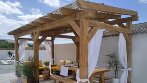 A wooden pergola with a table and chairs, surrounded by potted plants and a pool. - Condo Entero en Pantano de los Bermejales (Pantano de los Bermejales)
