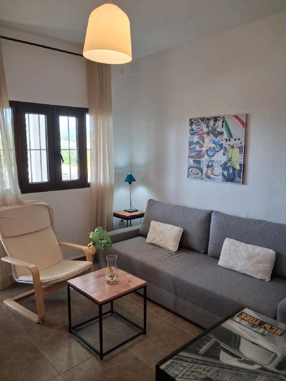 Una sala de estar con un sofá gris, una silla de madera, una mesita y una lámpara.