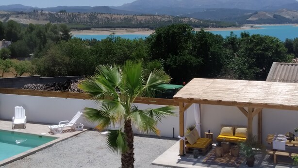A pool area with lounge chairs, a palm tree, and a view of a beach and mountains. - Condo Entero en Pantano de los Bermejales (Pantano de los Bermejales)