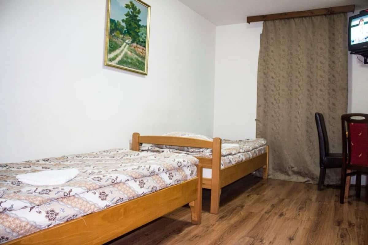 A room with a single bed, a chair, a television, and a painting on the wall.