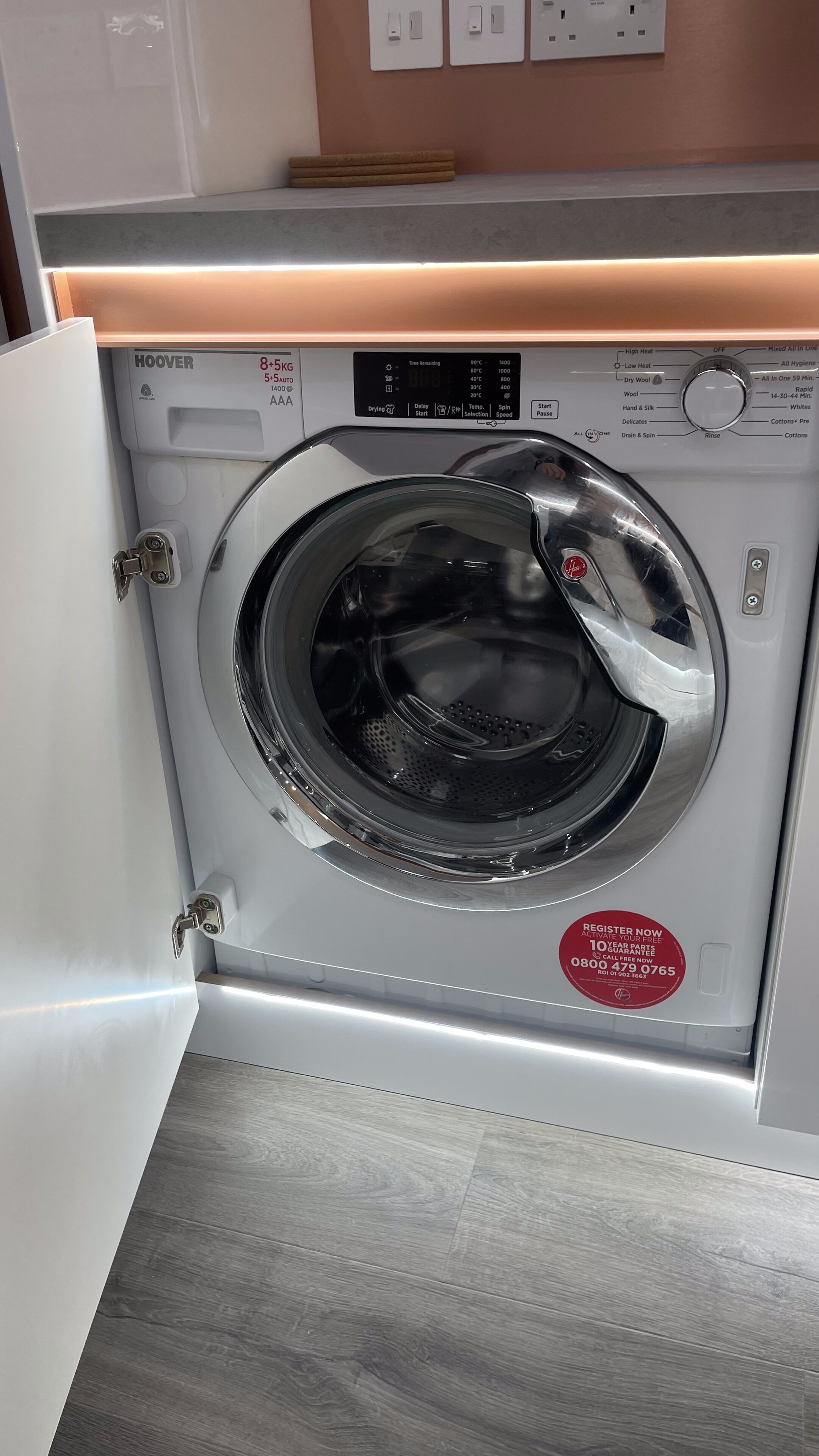 A front-loading washing machine with a digital display, a control panel, and a red sticker.