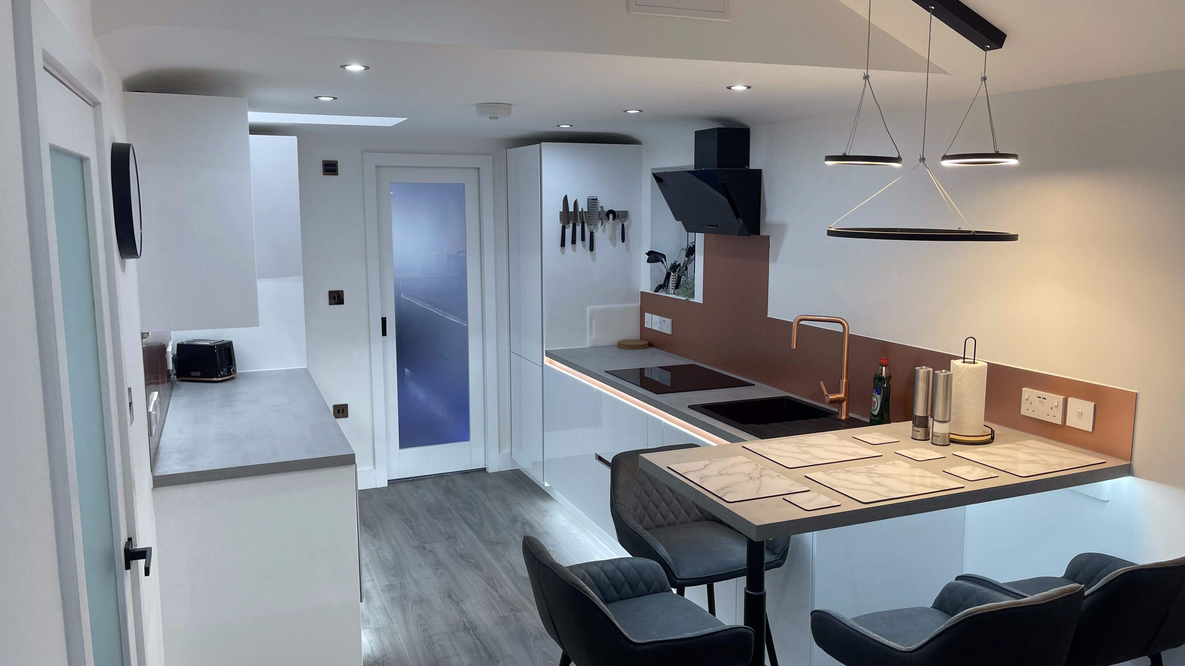A modern kitchen with a central island, black bar stools, and a view into the adjacent living area.
