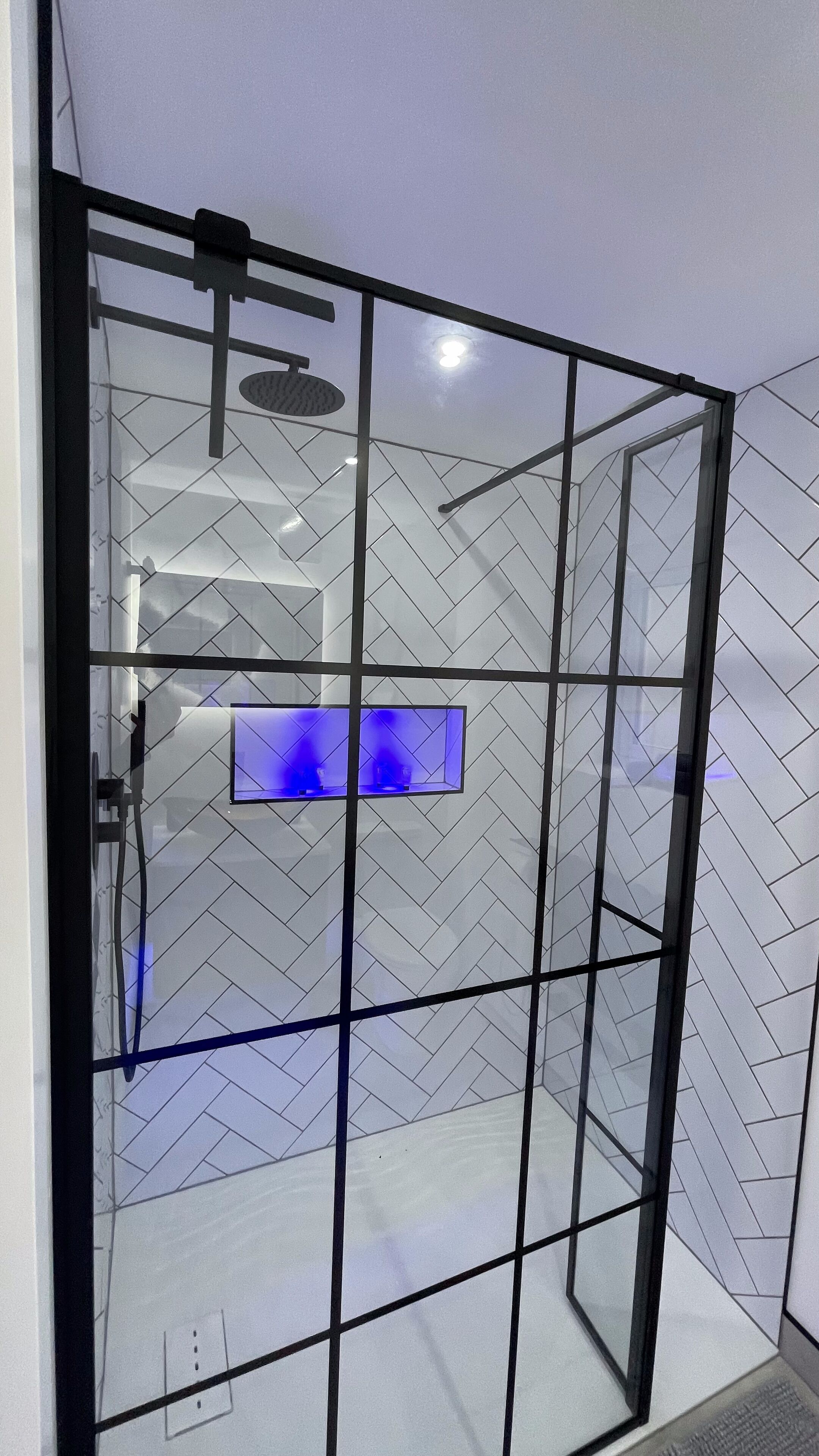 Een moderne badkamer met een glazen douchedeur, een douche en een blauw verlichte wastafel.
