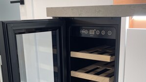 Kompakti jääkaappi, jossa on sisäänrakennettu viilennin viinipulloille, digitaalinen näyttö ja puinen viiniteline.