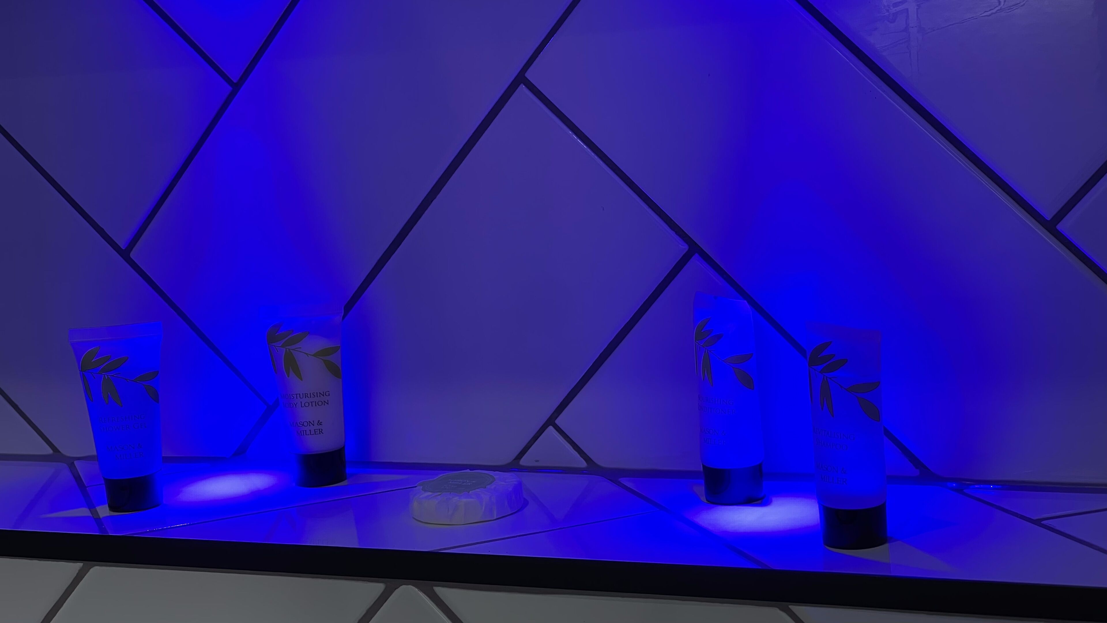 Ein Badezimmer mit einer blau beleuchteten Wand und drei Lotionflaschen auf einem Regal.