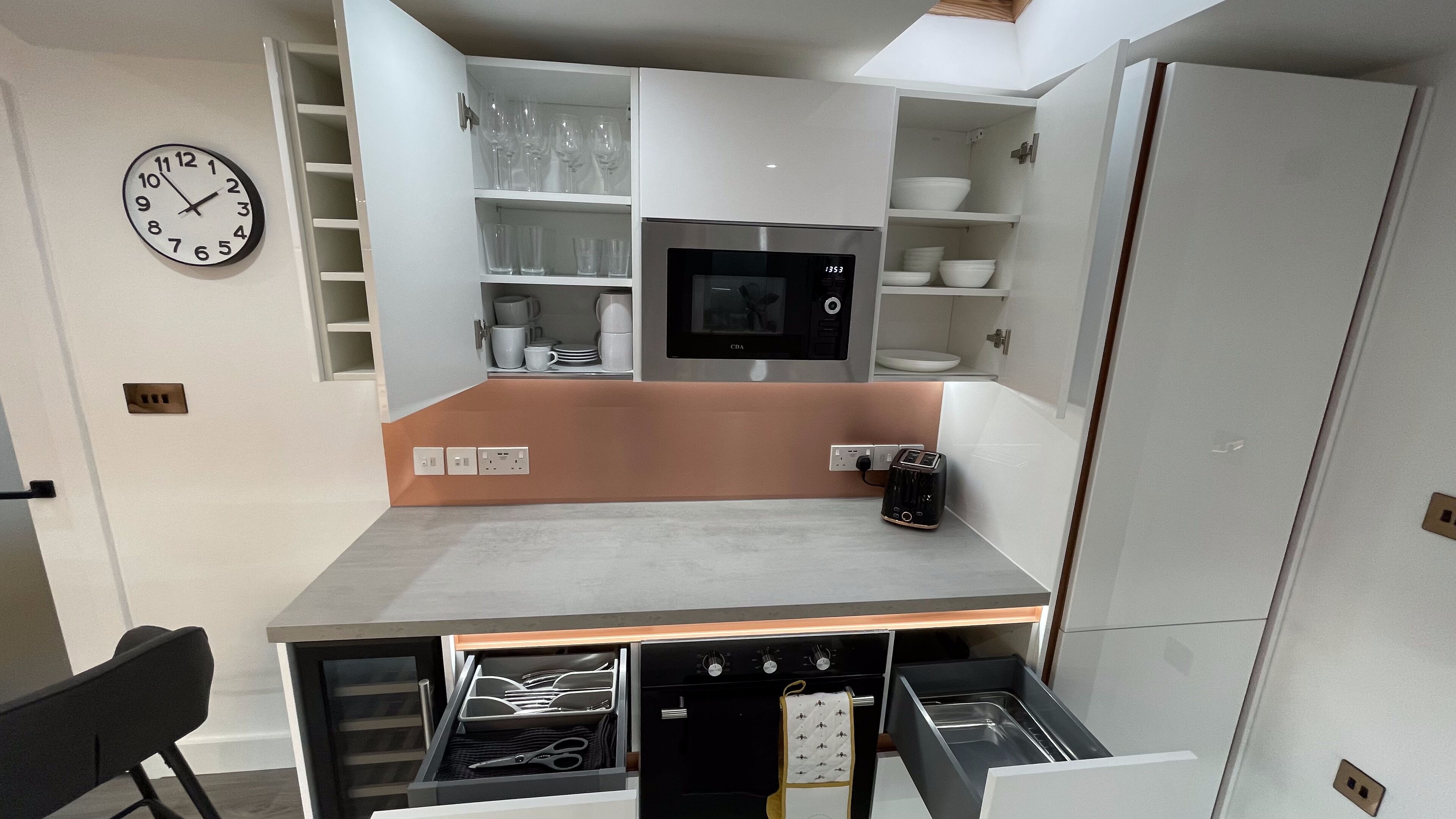 Une cuisine compacte équipée d’un four à micro-ondes encastré, d’une horloge et d’un plan de travail sur lequel se trouve un grille-pain.