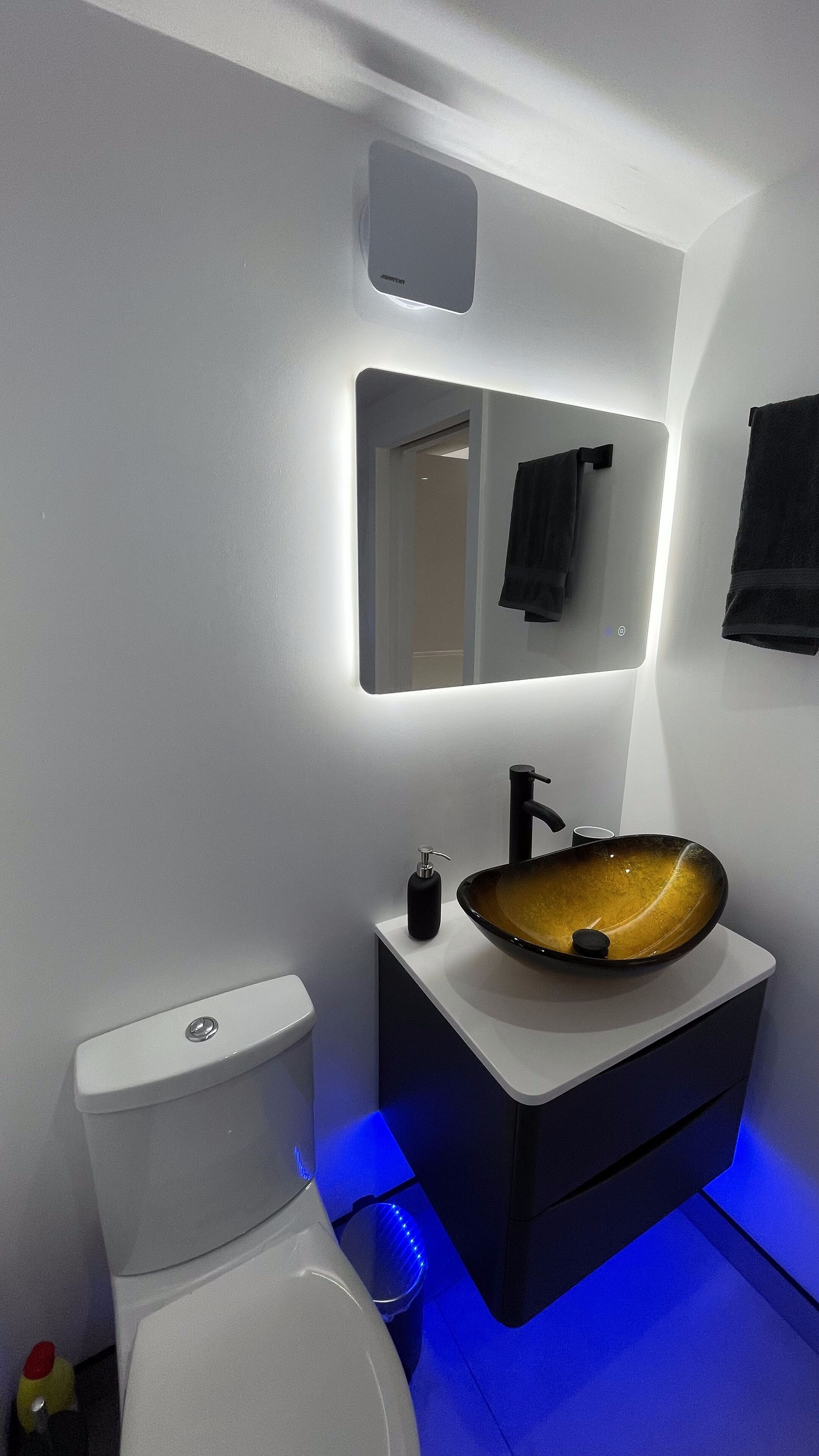 A modern bathroom with a white toilet, a black sink with a unique bowl design, and a mirror above the sink.