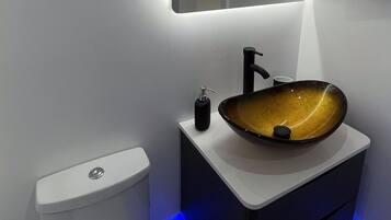 A modern bathroom with a white toilet, a black sink with a unique bowl design, and a mirror above the sink.
