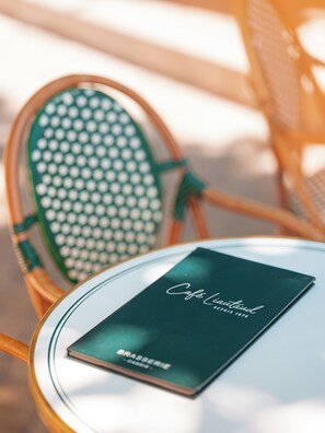A table with a menu titled "Cafe Land" and a chair with a green and white pattern. - Hôtel Liautaud Cassis by Germain Collection (Cassis)