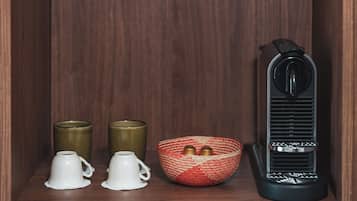 Una estantería con una radio negra, una cesta tejida con dos objetos metálicos y dos tazas blancas.