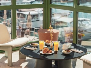 A round table with breakfast items, a vase with flowers, and a view of boats through large windows. - Hôtel Liautaud Cassis by Germain Collection (Cassis)